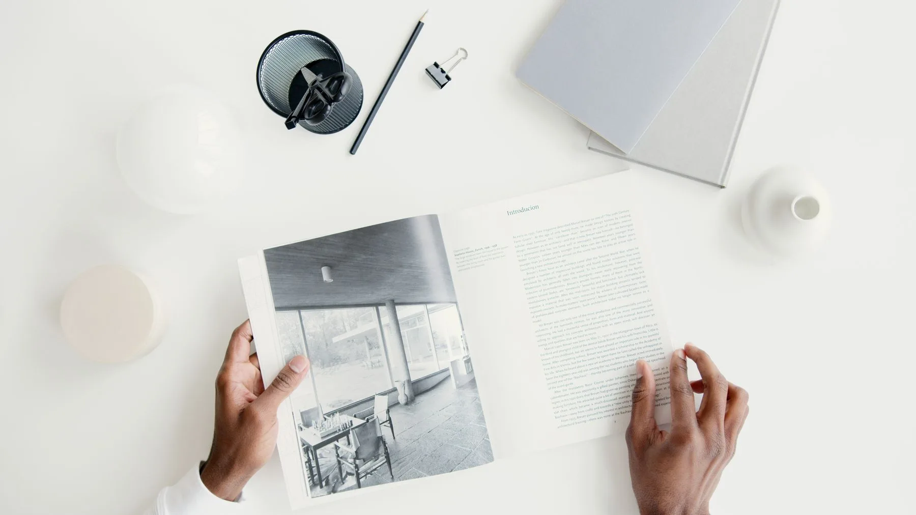 Hands holding an open magazine on a quiet white editing desk